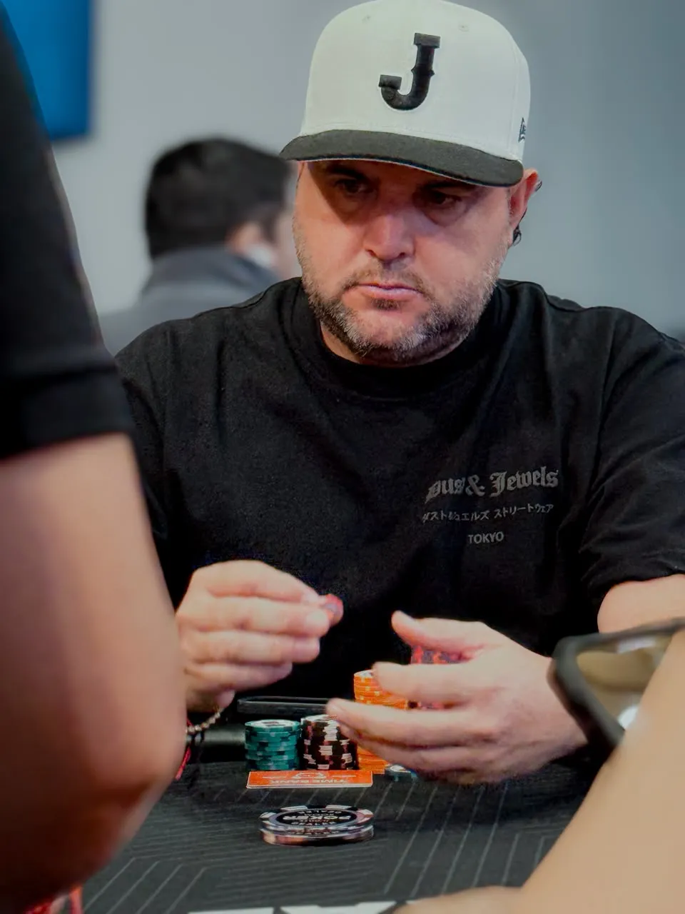 Joe.Pok3r con gorra blanca "J" apilando fichas en la mesa